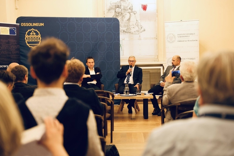 Zdjęcie sali, siedzących ludzi. W tle prelegenci.