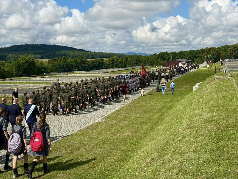 Zdjęcie przedstawia w przemarsz uczestników wydarzenia spod bramy obozu pod pomnik