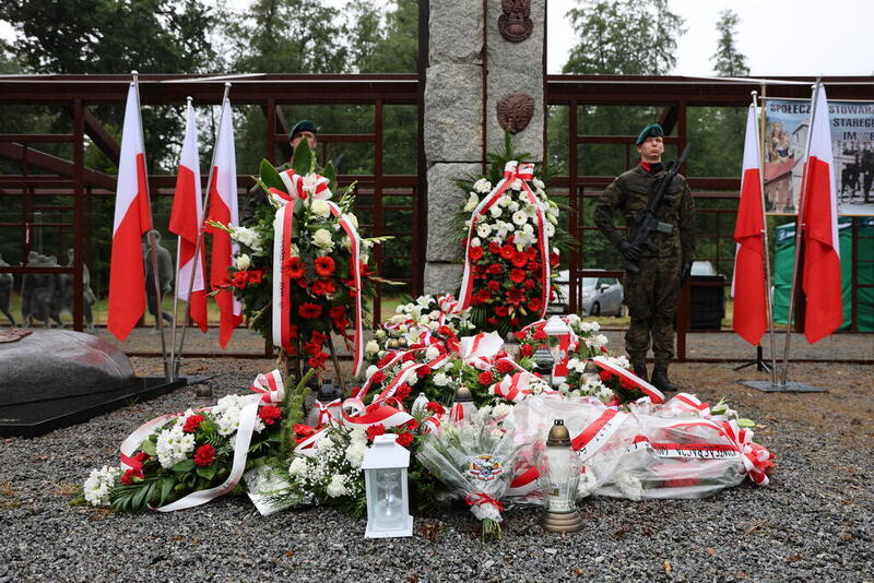 na zdjęciu miejsce pod krzyżem, gdzie złożono wiązanki kwiatów