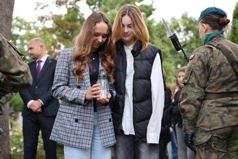 Zdjęcie prezentuje dwie uczennice składające znicz na grobie