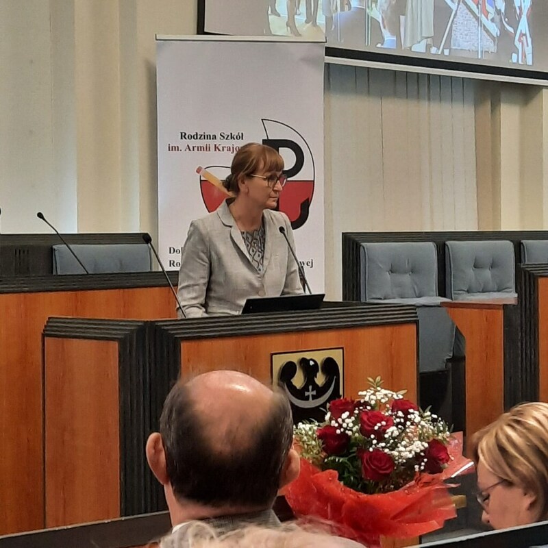 Zdjęcie przedstawia osobę, która stoi przy mównicy w trakcie wystąpienia