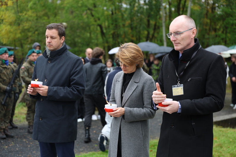 zdjęcie przedstawia moment składania zniczy, w środku dyrektor muzeum w Łambinowicach