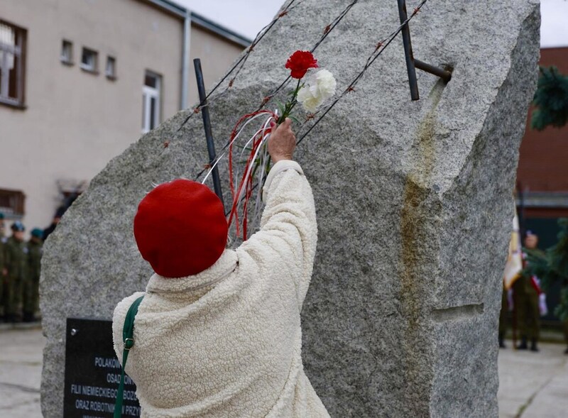 na zdjęciu kobieta, która wkłada pod obelisk różę