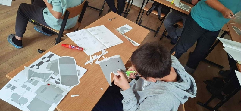 siedząca przy stole młodzież wycinająca model z kartonu