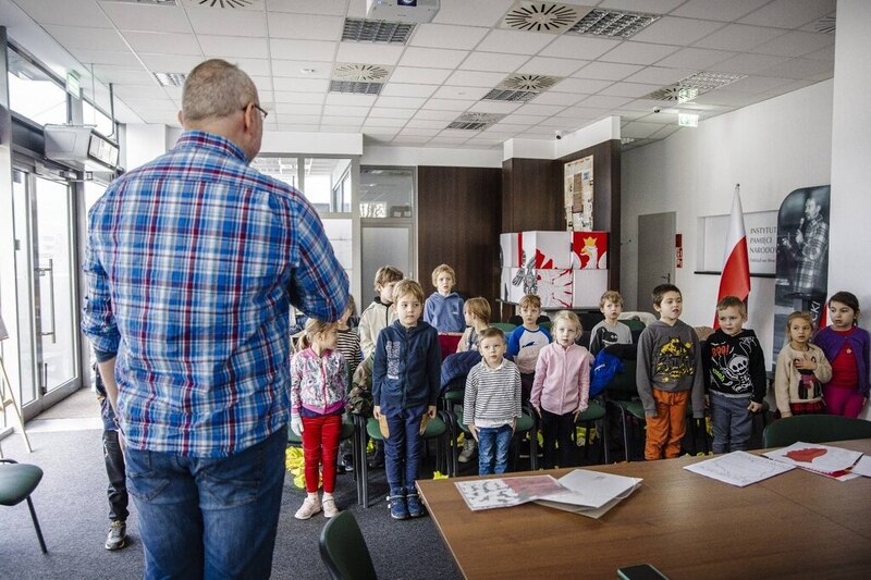 na pierwszym planie edukator, który pokazuje w jaki sposób stoi się podczas odgrywania hymnu państwowego