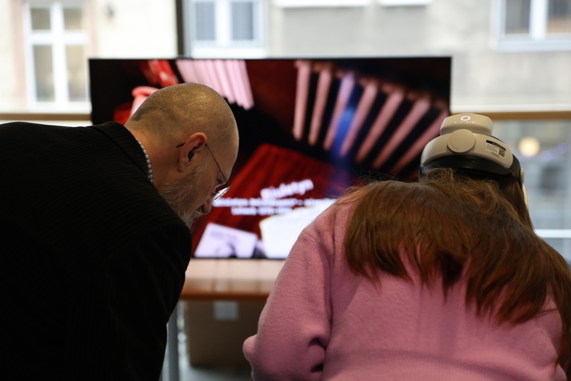 fragment pokazu możliwości VR IPN, dziewczyna w okularach VR przenosi się w czasie do mieszkania w czasie PRL. Szczegóły pokazuje telewizor w tle.