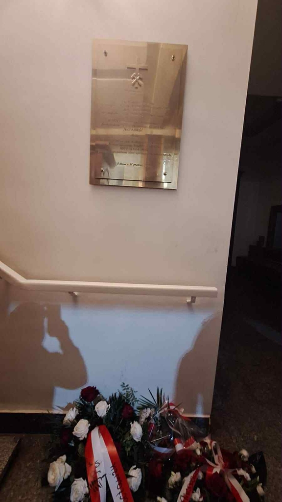 na zdjęciu tablica w kościele, pod tablicą kwiaty