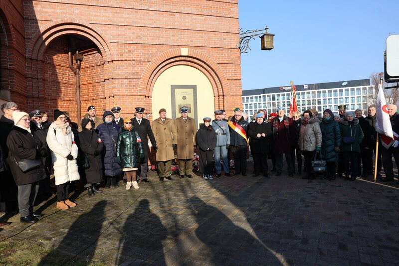 zdjęcie grupowe, uczestnicy spotkania stoją pod tablicą pamiątkową