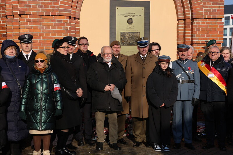 zdjęcie grupowe, uczestnicy spotkania stoją pod tablicą pamiątkową