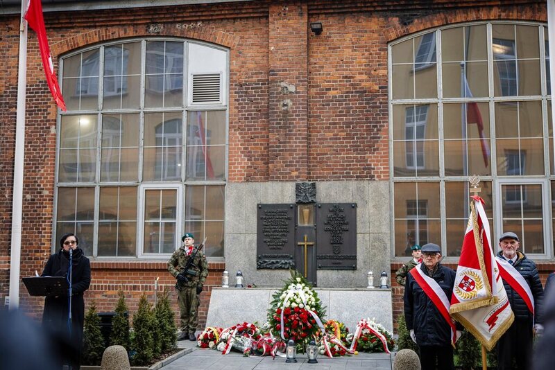 zdjęcie prezentuje tablicę pod którą składane były wiązanki kwiatów