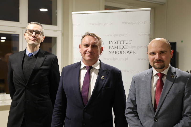 zdjęcie pamiątkowe, trzy osoby stojące na tle rollupa IPN