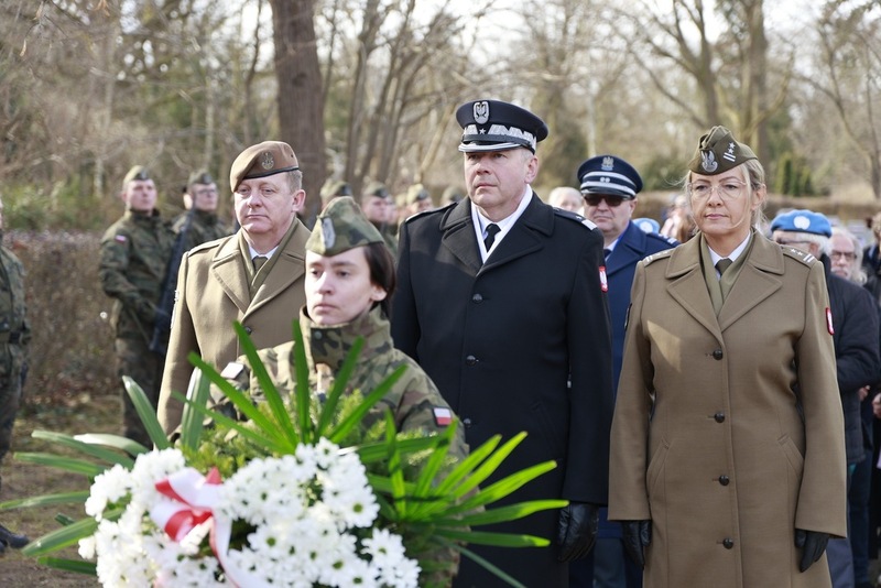 Moment składania kwiatów. W tle delegacja oficerów