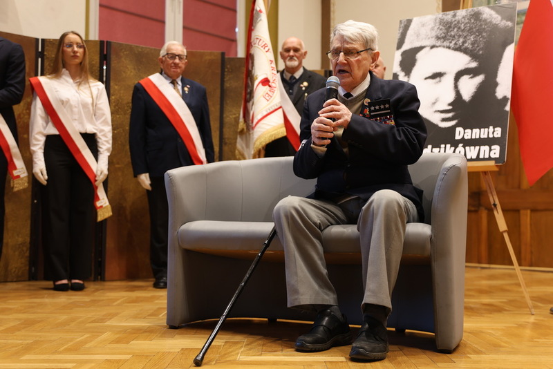 na scenie stoi kanapa, na kanapie siedzi z mikrofonem w ręce kpt. Wołczaski