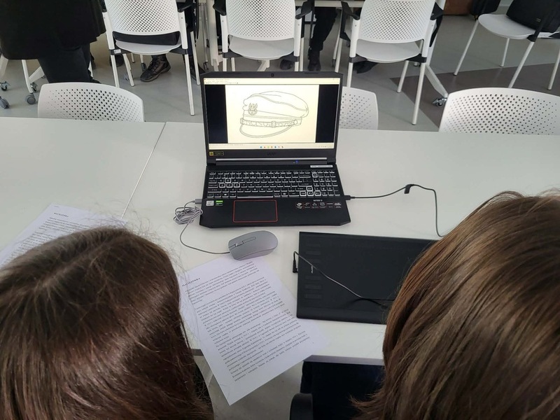 Widok na salę, na stole stoją komputery, gdzie młodzież realizuje zadania. Na środku prowadzący zajęcia Artur Cieślik