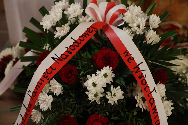 zdjęcie pokazuje wieniec kwiatow ze wstęgą IPN