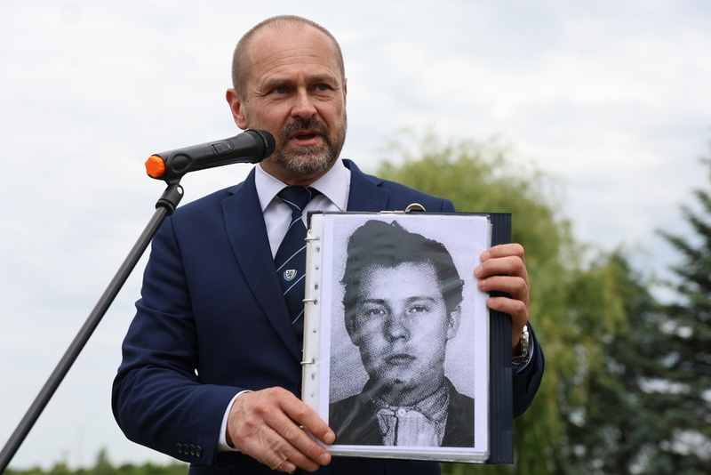 przy mikrofonie stoi regionalista ze zdjęciem bohatera